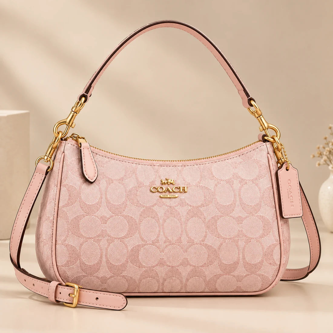 A light pink Coach handbag with the brand's signature monogram pattern, gold-tone hardware, and a top handle, shown on a neutral beige background.