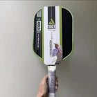 A hand holding a green and black electric fly swatter against a plain gray wall.
